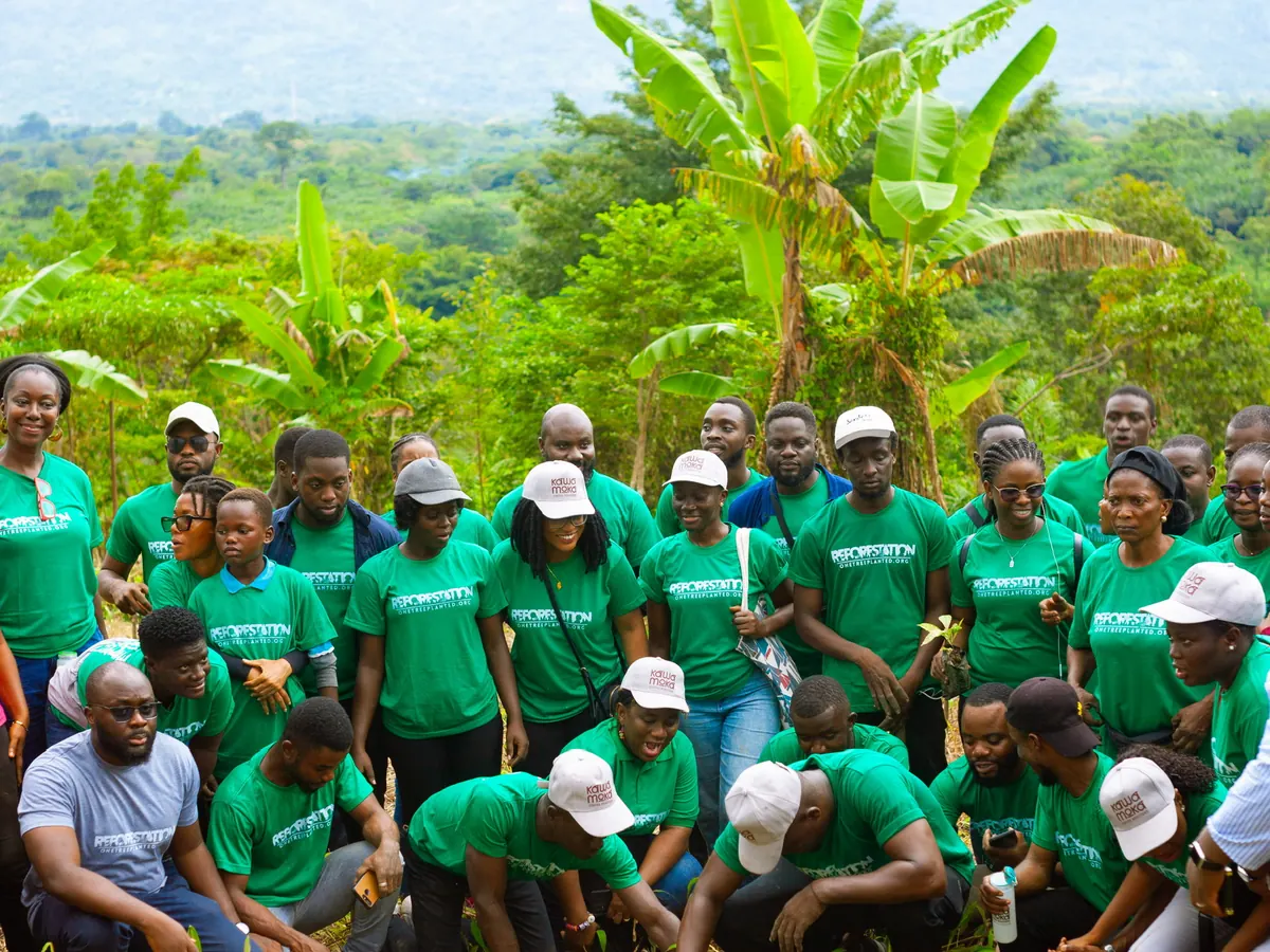 A large group in green reforestation T-shirts gathers on a hillside farm in Ghana during a tree planting day