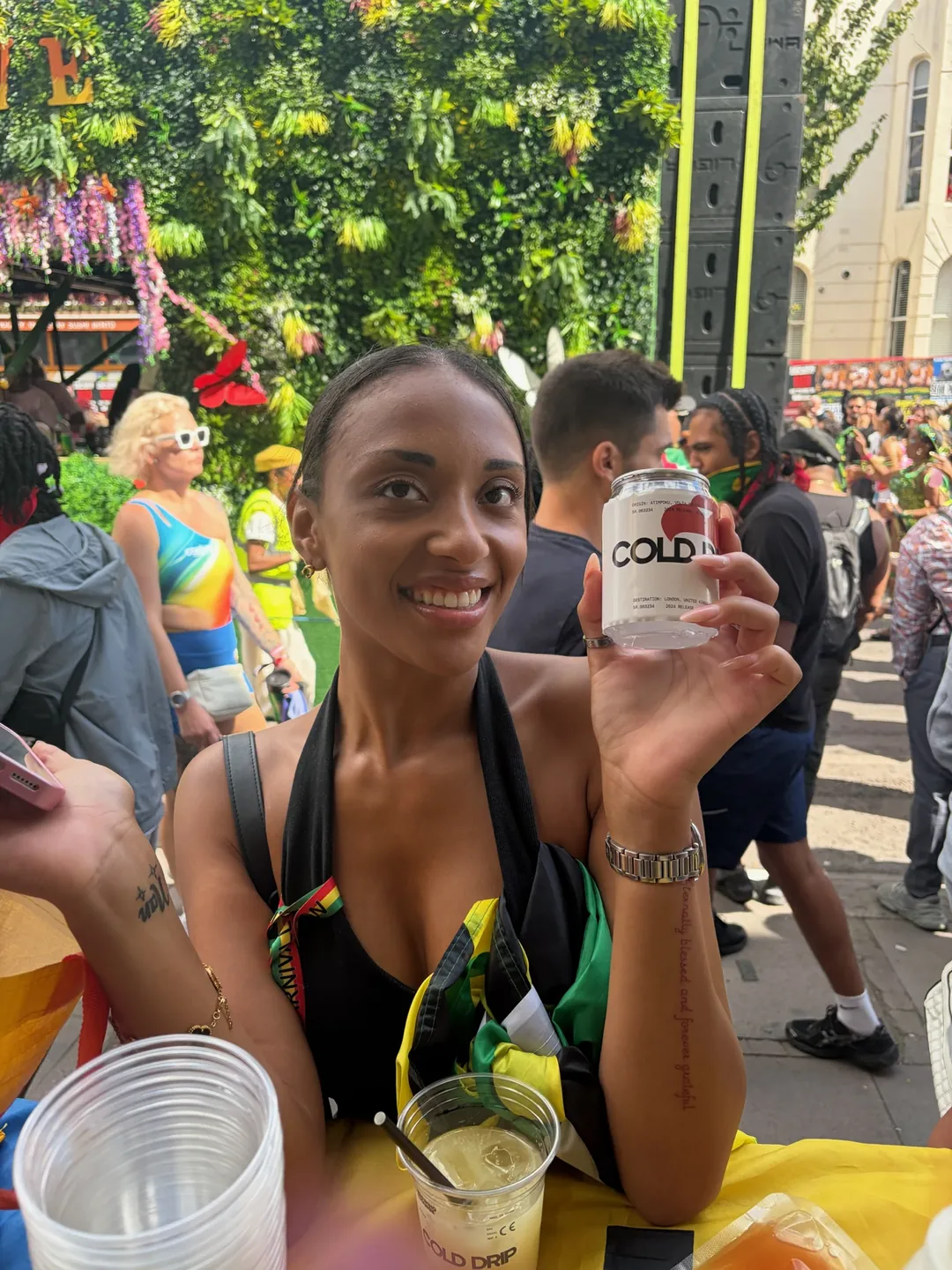 A smiling woman holds up a can of Brewing Change Cold Drip at a busy summer street carnival